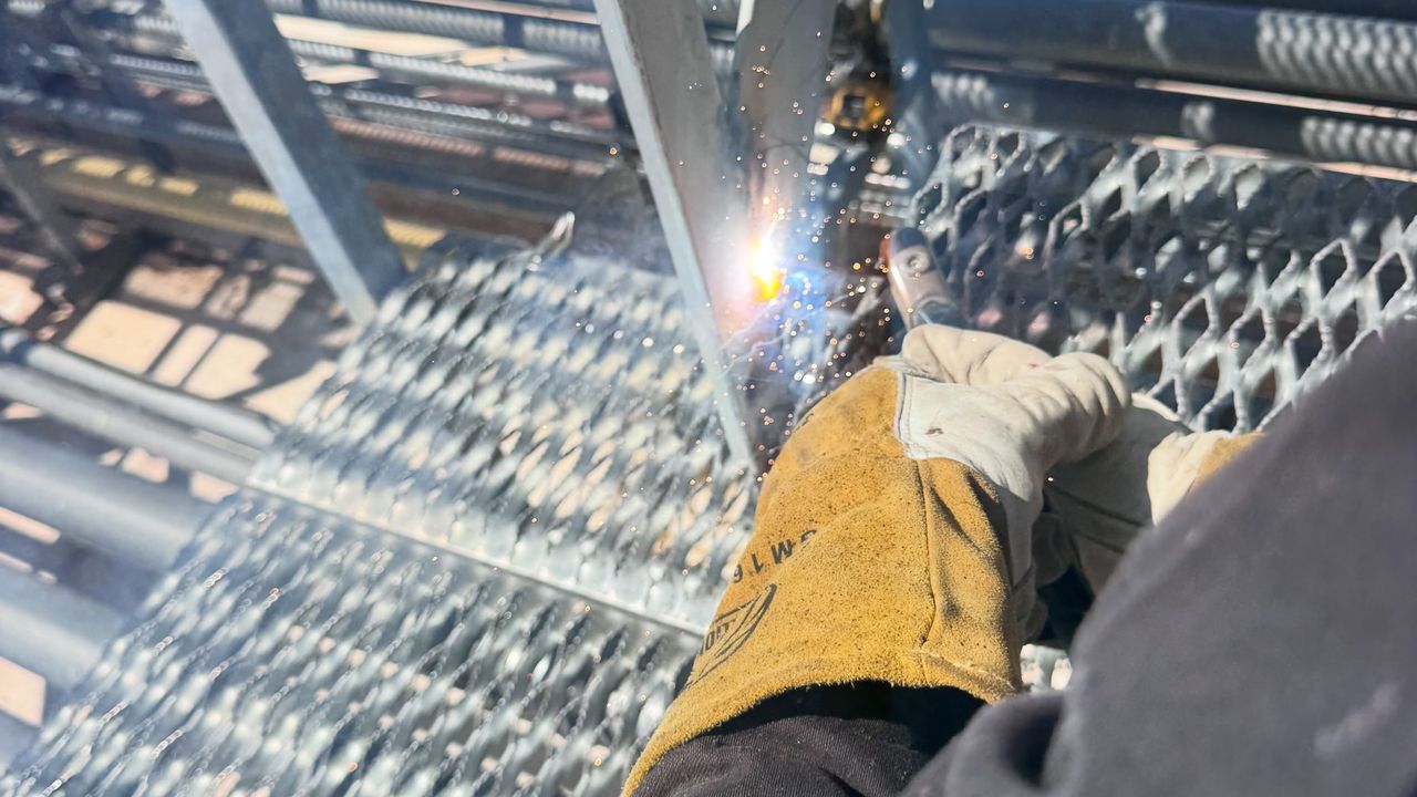Close on a gloved hand welding a joint on galvanized catwalk grating.