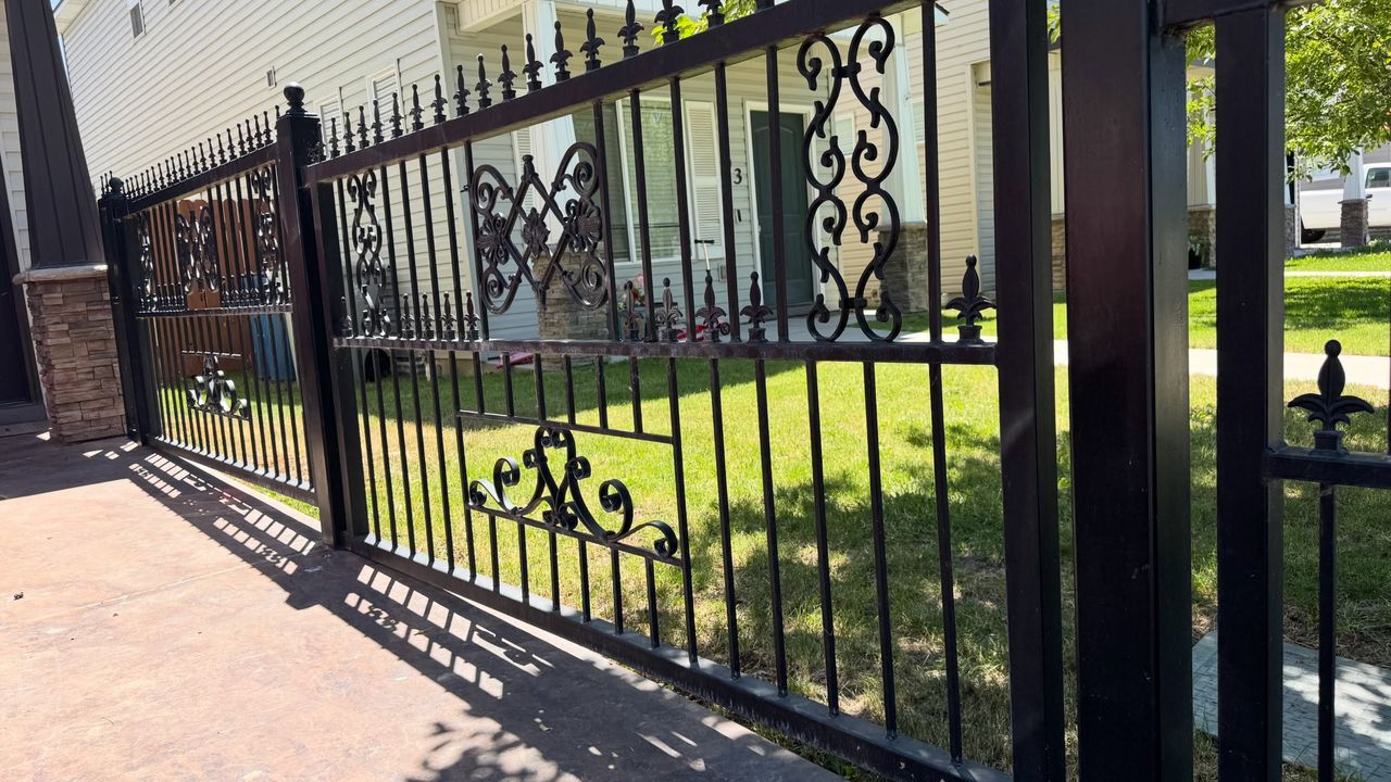 A black ornamental iron fence and gate with scroll panels along a front lawn.