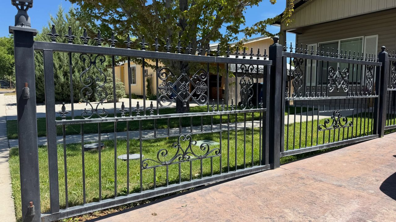 A black ornamental iron fence and gate with scrollwork panels, along a stamped concrete drive.