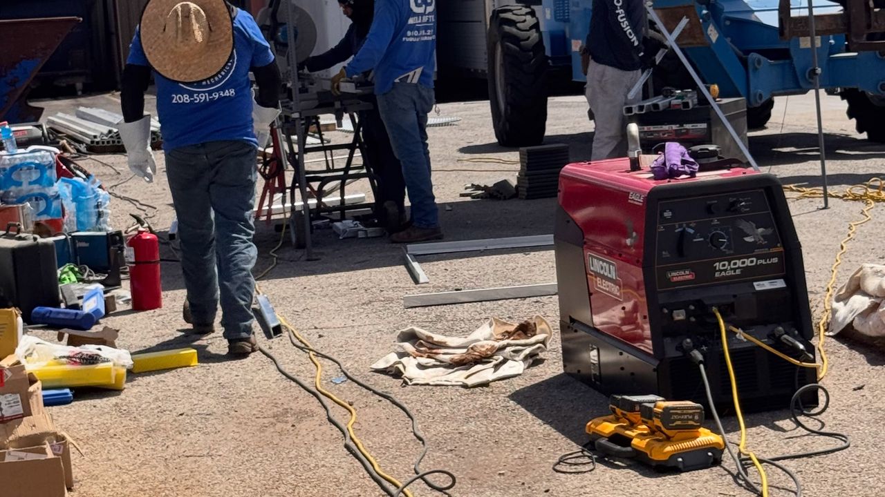 The crew in blue Pro-fusion shirts working under a canopy on a lot, welding machine and stands around them.