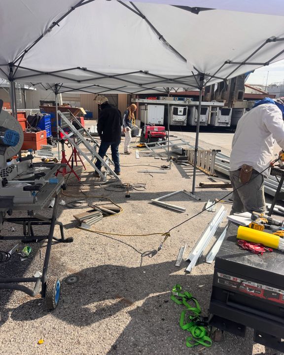 The crew working under a canopy on a lot, stair frames and tools around them.