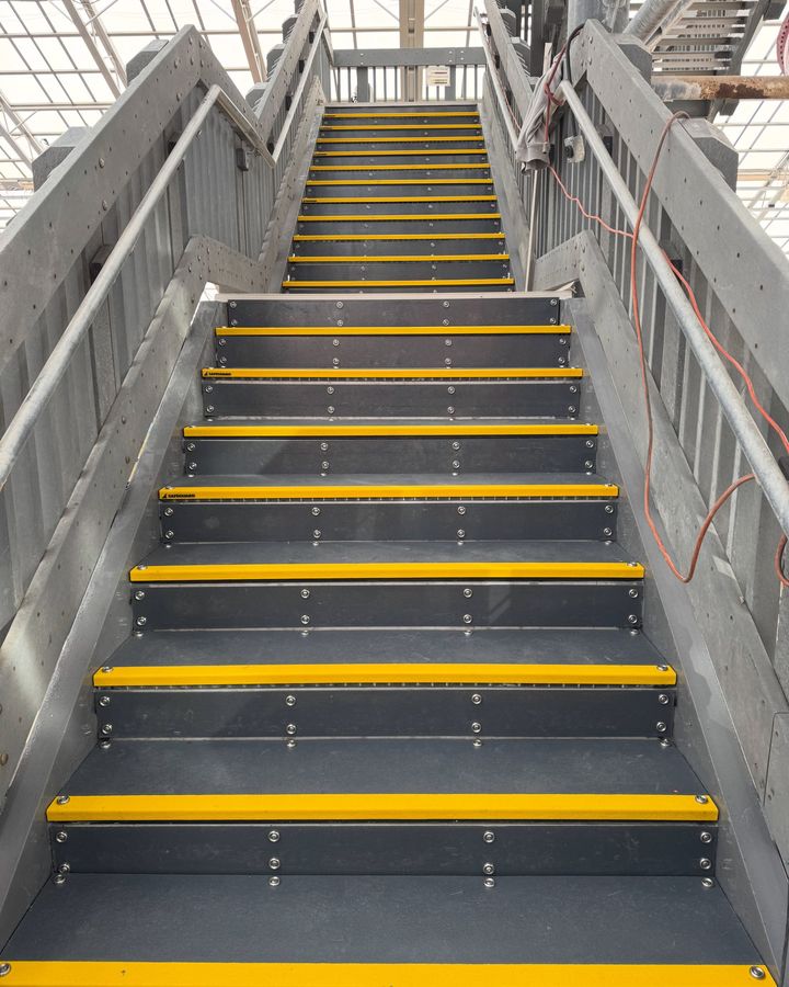 A tall run of new grey steps with bright yellow nosing, rising between handrails.